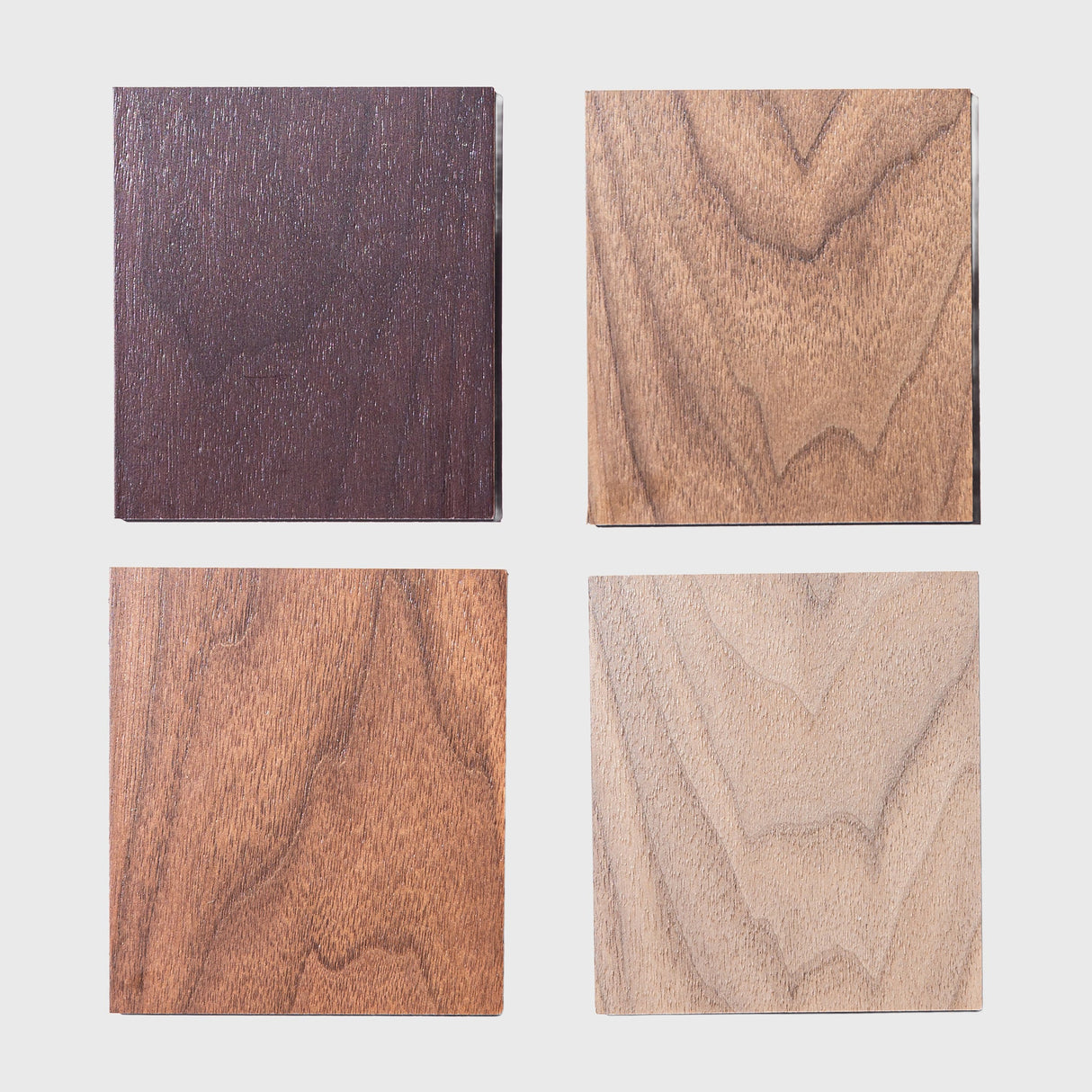 Four walnut wooden squares of different finishes on a white background