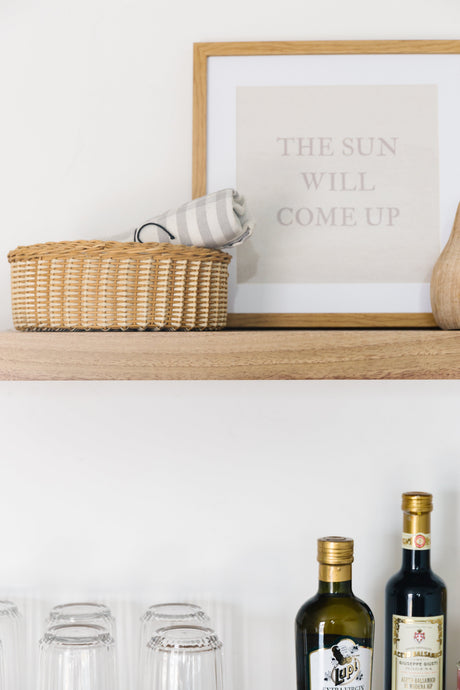 Walnut floating shelves with the bleached finish applied decorated with glass cups, oils, wooden basket with towel, photo frame, and a wooden vase